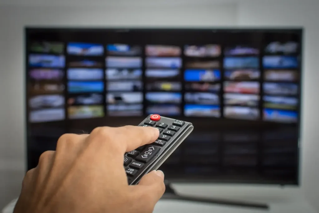 Close-up of hand holding remote control in front of IPTV Smarters Pro interface on TV screen – UAE subscription IPTV