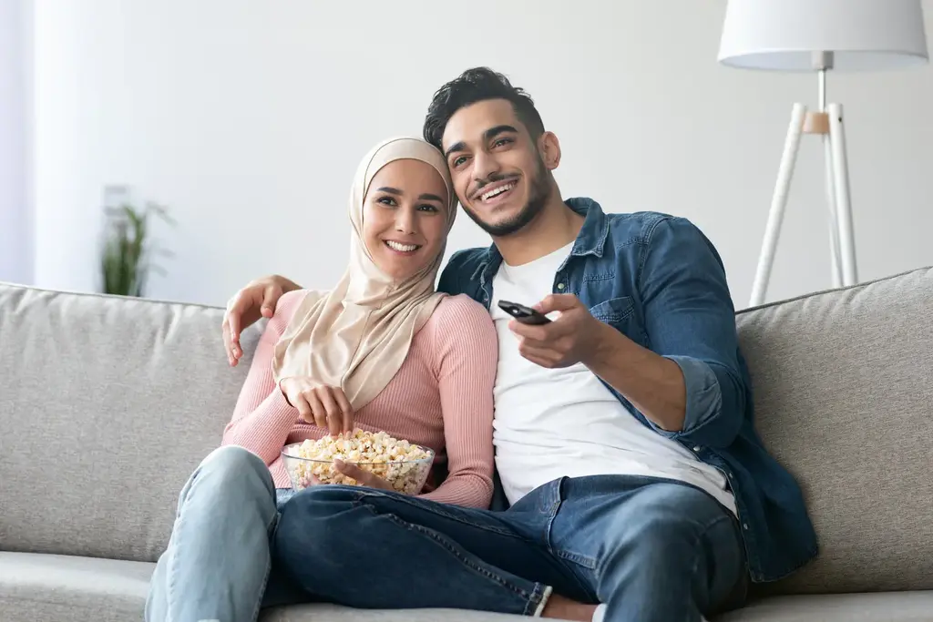 Happy couple watching IPTV Smarters Pro at home with remote control and popcorn – best IPTV UAE